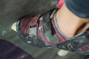 Fotografía detalle del pie de una mujer con una zapatilla de escalada en un rocódromo